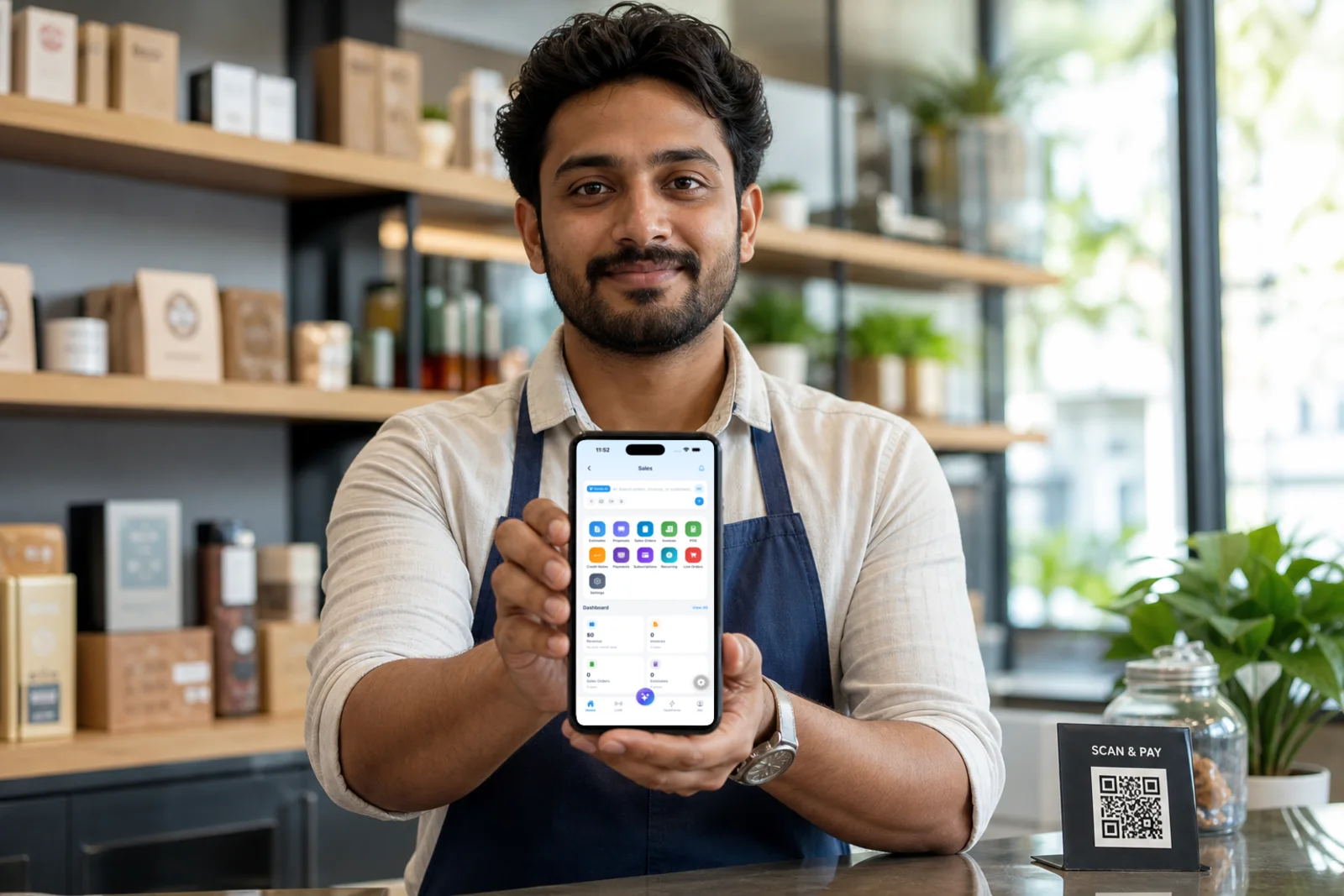 A shopkeeper behind the counter holding a phone showing the Kardopal Sales screen.